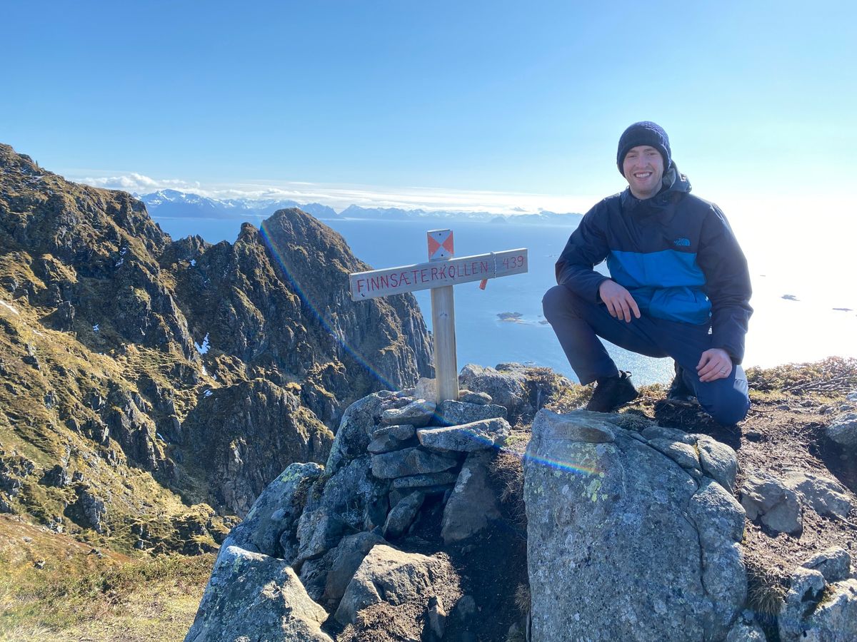 Scott smiling at the summit of Finnsæterkollen in Norway, with mountains and sea behind him